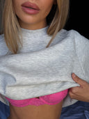 Grey melange crew neck sweater, close-up of the crew neck and soft brushed knit, lifted to show a pink bra