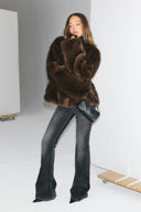 Brown faux fur loose-fit jacket worn fur side out, styled with grey flared jeans in a white studio