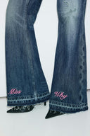 Close-up of dark vintage blue wide-leg jeans with pink "Miss Why" hem embroidery and raw hems