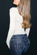Off-white sheer turtleneck body with long sleeves, tucked into blue jeans, back view on model