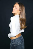 Cream tight-fit drapey top with long sleeves and cropped hem, back view on model looking over the shoulder
