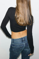 Black cropped top with long sleeves and a hem at the waist, back view on model