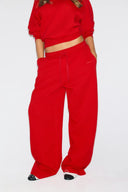 Red loose-fit low-waist sweatpants with drawstring and baggy leg, front view on model with a matching sweatshirt