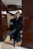Black faux fur coat with shaggy collar and cuffs, styled with grey jeans in a wood-panelled lobby