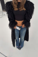 Black faux fur coat with shaggy cuffs and front trim, styled with a black crop top in a studio