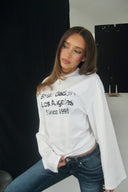 Off-white loose-fit crew neck top with wide long sleeves and text print, front view on model in a photo studio