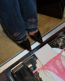 Close-up of dark vintage blue jeans hem with pink "Miss Why" embroidery and raw edges