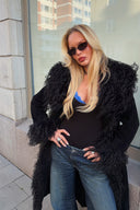 Black faux fur coat with shaggy collar and cuffs, styled with blue jeans on a city street