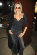 Black padded bodysuit with deep neckline and 3/4 sleeves, styled with grey flared jeans in a hotel lobby