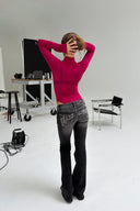 Berry boost (pink) sheer turtleneck body with long sleeves, styled with black flared jeans, back view in a photo studio