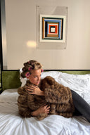 Tiger print faux fur jacket with long sleeves, styled with dark jeans on a hotel bed