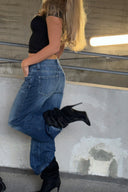 Dark blue loose-fit low-waist wide-leg jeans, styled with black heeled boots in a parking garage