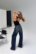 Black ribbed tight-fit sleeveless body with racer back, styled with wide blue jeans, in a white photo studio