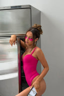 Cerise (pink) figure-hugging bodysuit with padded cups and deep neckline, side view on model by an open fridge