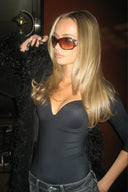 Black figure-hugging padded bodysuit with deep neckline, styled with a black faux fur coat in a dim interior