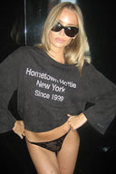 Washed black loose-fit crew neck top with long sleeves and text print, styled with a black lace thong in a dark room