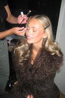 Dark brown faux fur coat with shaggy collar, styled with a black top backstage at a makeup table
