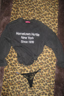Washed black crew neck top with long sleeves and text print, laid flat with a black lace thong on a leopard print rug