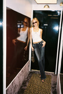 Black loose-fit low-waist bootcut tall jeans, styled with a white tank top, full-length in a mirrored hallway