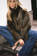 Brown faux fur loose-fit jacket worn fur side out, styled with blue flared jeans, seated on stairs