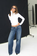Dark blue loose-fit low-waist wide-leg jeans, styled with a white long sleeve top in a photo studio
