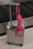 Wild orchid (pink) lace push-up bra with rhinestone straps, hanging on a silver suitcase at a baggage carousel