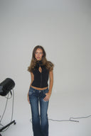 Black tight-fit keyhole top with keyhole cutout and high collar, styled with blue flared jeans, in a white photo studio