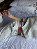 Grey melange crew neck sweater bunched at the waist over matching sweatpants, styled on a hotel bed