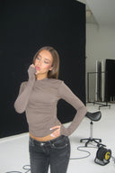 Grey tight-fit drapey top with ruched front and long sleeves, styled with black jeans in a photo studio