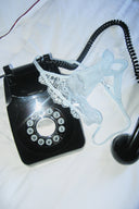 Blue lace thong with scalloped lace trim, laid on a black rotary phone on white bedsheets
