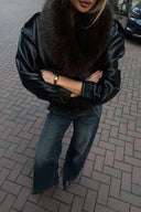 Black faux leather baggy jacket with brown faux fur collar, styled with wide-leg jeans on a brick street