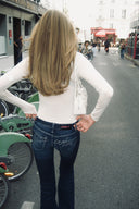 Off-white sheer turtleneck body with long sleeves, styled with blue flared jeans, back view on a city street