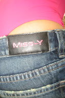 Close-up of a Miss Y logo patch on blue jeans, with the cerise (pink) bodysuit visible above the waistband