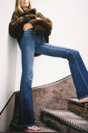 Dark blue low-waist bootcut jeans with flared full-length legs, styled with a brown faux fur jacket on a staircase