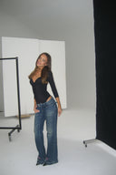Black padded bodysuit with deep neckline and 3/4 sleeves, styled with blue wide-leg jeans in a photo studio