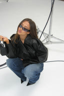Black faux leather baggy jacket worn without the faux fur collar, styled with blue jeans in a photo studio
