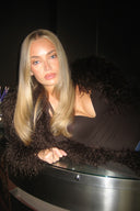Dark brown bodysuit with deep neckline, styled with a brown faux fur coat, leaning on a bar counter
